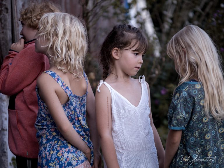 Vier Kinder in farbenfroher Kleidung stehen zusammen in einem grünen Garten und blicken nachdenklich zur Seite – © Axel Hebenstreit