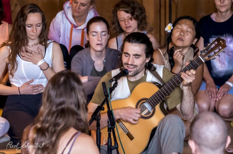 Musiker mit Gitarre umgeben von meditierenden Menschen in entspannter Festivalatmosphäre – © Axel Hebenstreit
