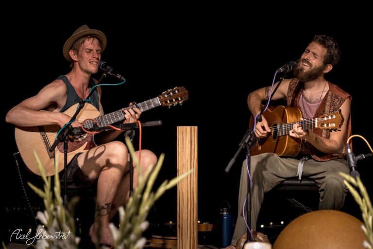 Zwei Musiker spielen leidenschaftlich akustische Gitarren auf einer Bühne, umgeben von einer stimmungsvollen Atmosphäre. – © Axel Hebenstreit