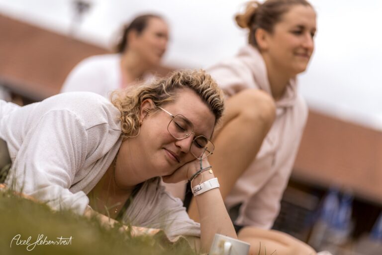Die entspannte junge Frau liegt auf dem Gras und genießt die Zeit im Freien während einer Yogaveranstaltung – © Axel Hebenstreit