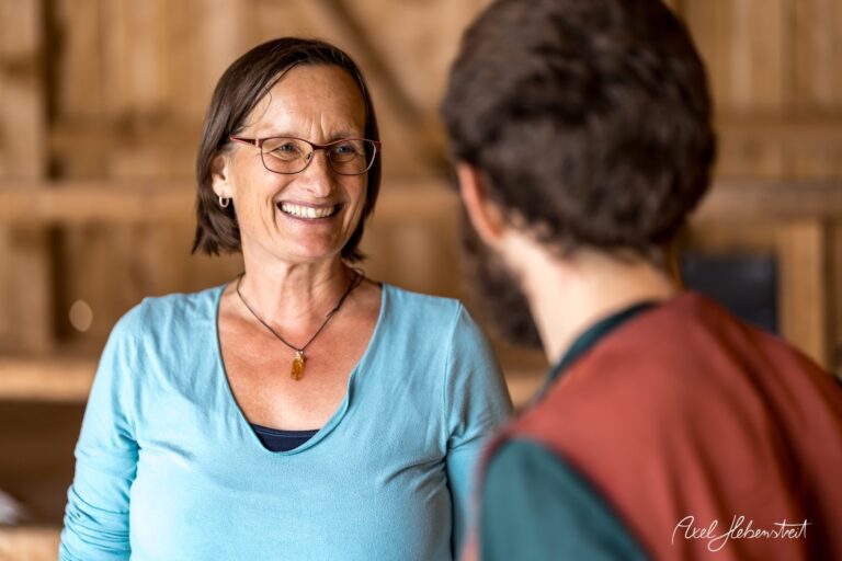 Lächelnde Frau im Gespräch mit einem Mann, entspannte Atmosphäre in rustikalem Holzinterieur – © Axel Hebenstreit