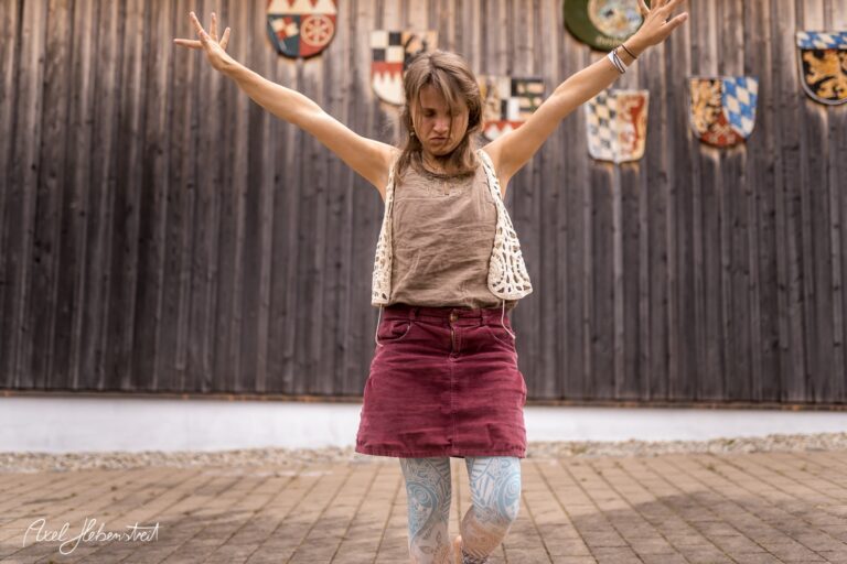 Frau in dynamischer Pose vor einer Holzwand mit Wappen, die Energie und Freude ausstrahlt – © Axel Hebenstreit