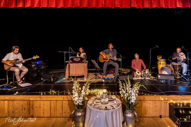 Musiker in einem abwechslungsreichen Setup spielen live auf einer Bühne, umgeben von stimmungsvoller Beleuchtung – © Axel Hebenstreit