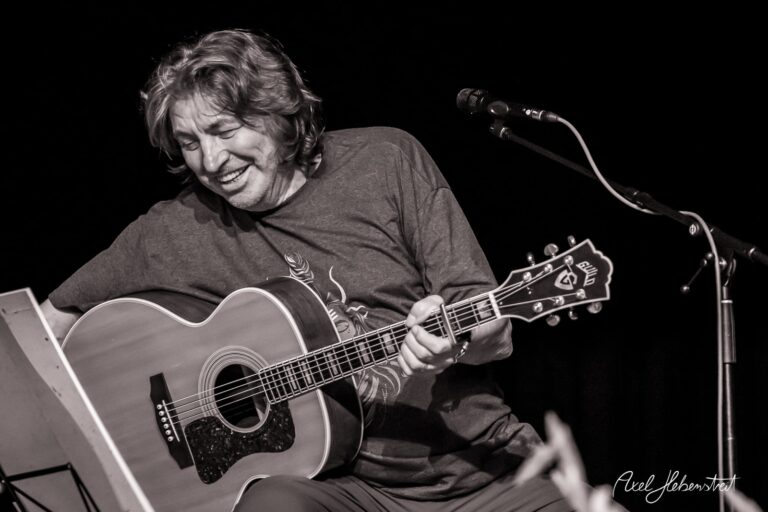 Lachender Musiker mit Gitarre auf der Bühne, der in ein intensives Konzert spielt – © Axel Hebenstreit