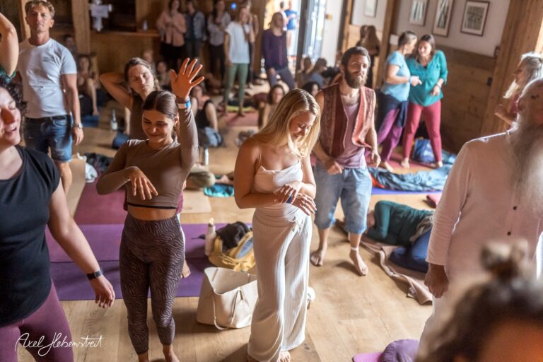 Verschiedene Menschen tanzen und meditieren in einem hellen Raum während eines Yoga-Events – © Axel Hebenstreit