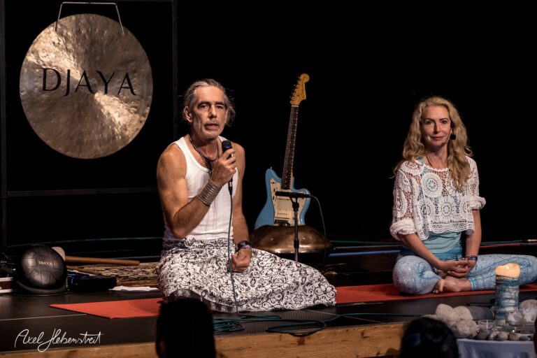 Zwei yogabegeisterte Menschen sitzen auf Matten, während im Hintergrund eine Gitarre und eine Klangschale stehen – © Axel Hebenstreit