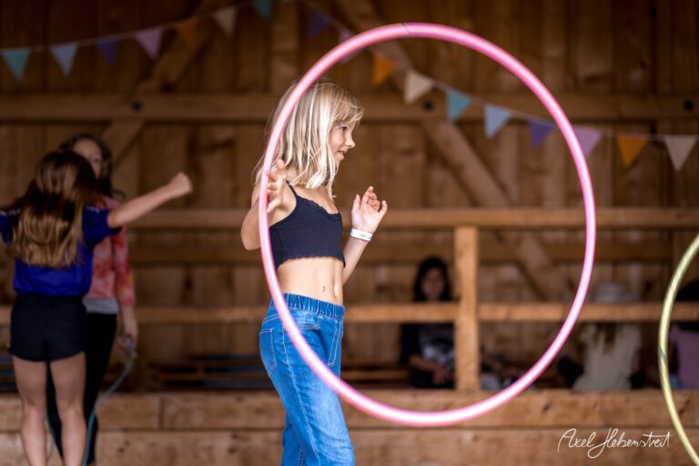 Ein Mädchen jongliert fröhlich mit Hula-Hoops in einem rustikalen Raum während eines Festivals – © Axel Hebenstreit