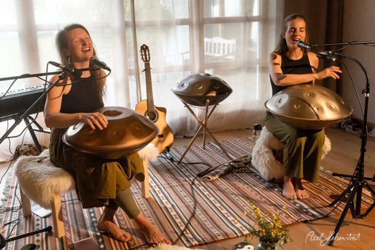 Zwei Musikerinnen spielen Handpan-Trommeln und singen bei einer intimen Wohnzimmer-Session