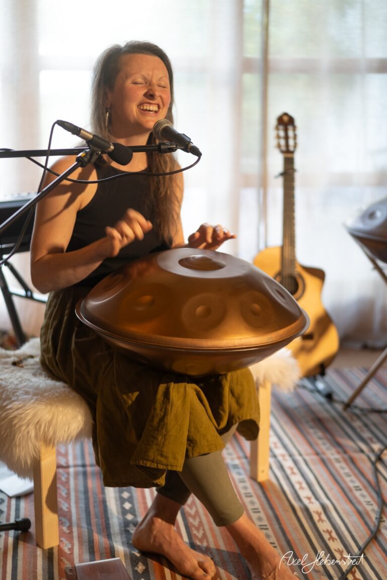 Musikerin singt leidenschaftlich und spielt Handpan in einem hellen, sonnendurchfluteten Raum