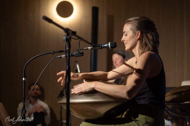 Musikerin spielt konzentriert am Schlagzeug während eines intimen Live-Auftritts im warmen Bühnenlicht.