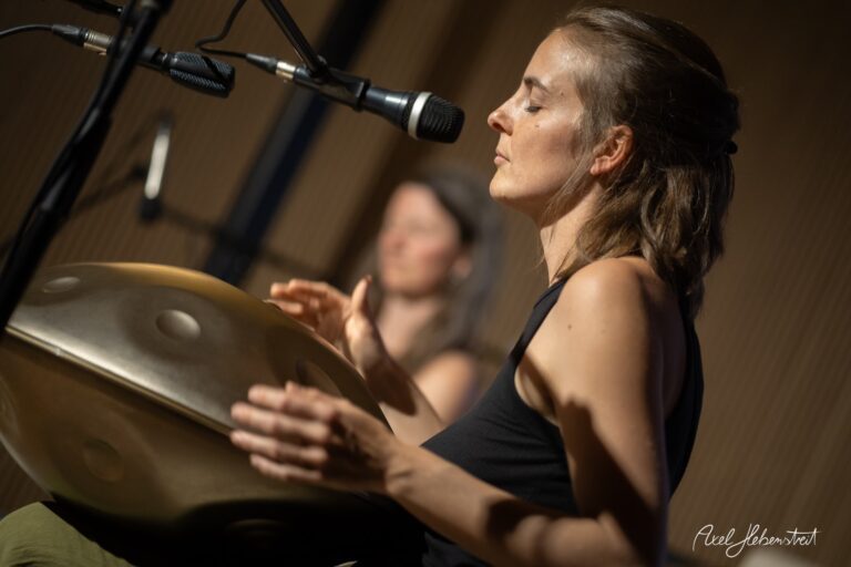 Musikerin spielt konzentriert Handpan während eines Live-Auftritts vor Mikrofonen