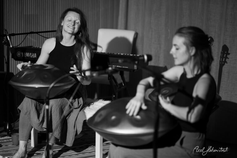 Zwei Musikerinnen spielen konzentriert Handpan-Trommeln in einem Yogastudio in schwarz-weiß Aufnahme.