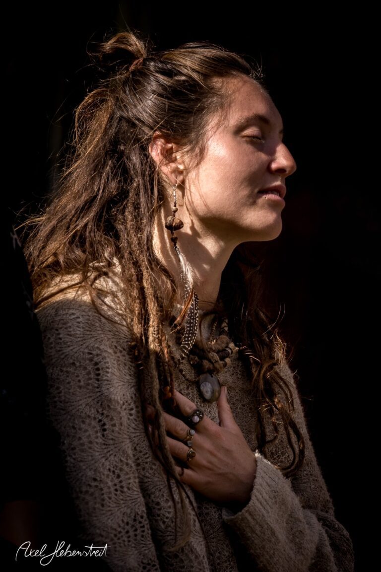 Eine nachdenkliche Frau mit Dreadlocks und Schmuck, die meditativ in das Licht blickt – © Axel Hebenstreit
