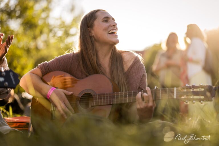 Eine fröhliche Frau spielt Gitarre und singt in einer natürlichen Umgebung bei Sonnenuntergang – © Axel Hebenstreit