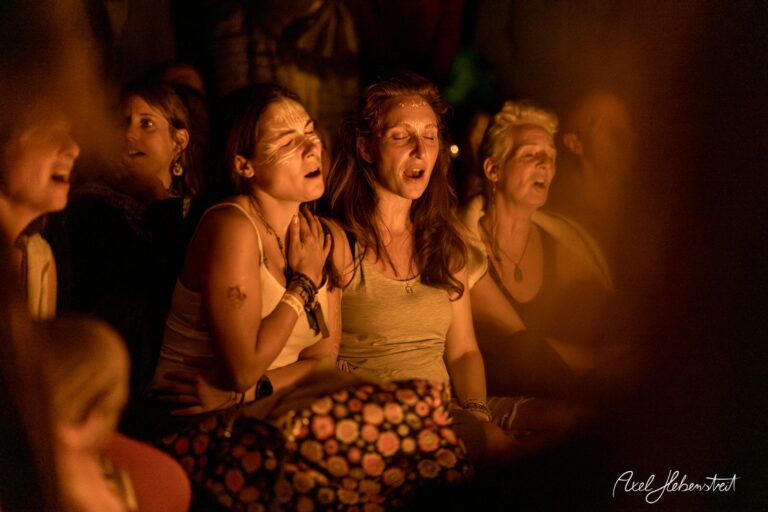 Zwei Frauen in einem meditativen Moment, umgeben von einer Gruppe, strahlen Freude und Verbundenheit aus – © Axel Hebenstreit