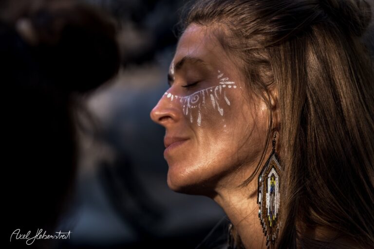 Porträt einer Frau mit dekorativen Gesichtsmustern und Ohrringen, die in einem entspannten Moment innehält – © Axel Hebenstreit