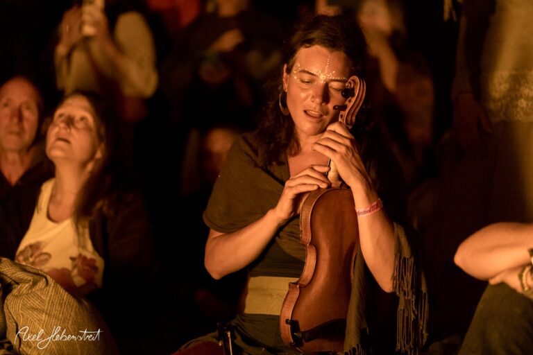 Frau spielt mit geschlossenen Augen eine Geige in einer warmen, festlichen Abendatmosphäre – © Axel Hebenstreit