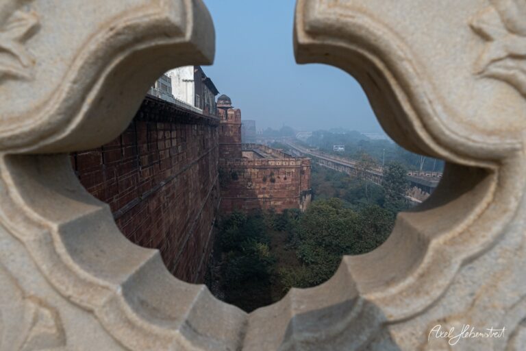 Blick durch ein kunstvoll gestaltetes Fenster auf die Mauer eines historischen Forts in nebliger Umgebung – © Axel Hebenstreit