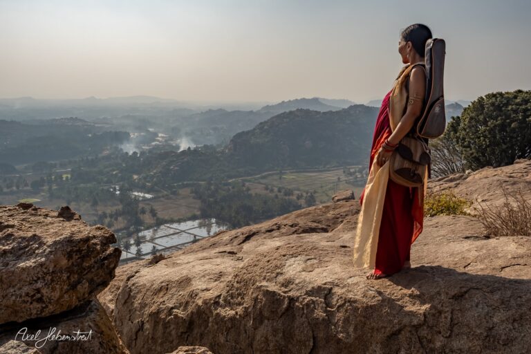 Frau in traditioneller Kleidung mit Instrument blickt über eine malerische Landschaft – © Axel Hebenstreit