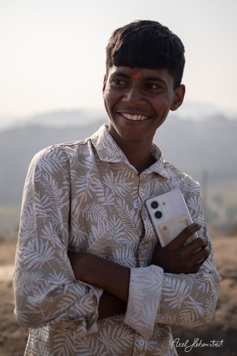 Ein lächelnder Junge mit einem Smartphone, umgeben von einer sonnigen Landschaft. – © Axel Hebenstreit