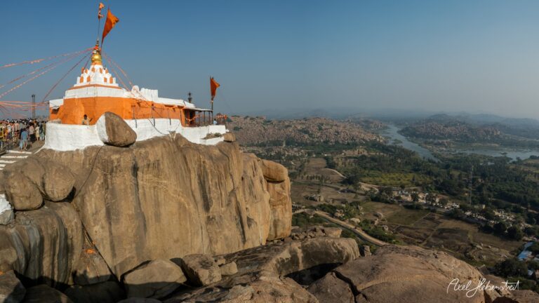 Blick auf einen Tempel auf einem Felsen mit orangefarbenen Flaggen, umgeben von einer malerischen Landschaft – © Axel Hebenstreit
