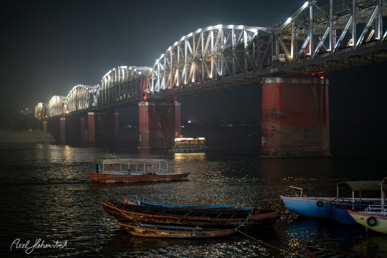 Beleuchtete Brücke über den Fluss mit Booten im Vordergrund in nächtlicher Stimmung – © Axel Hebenstreit