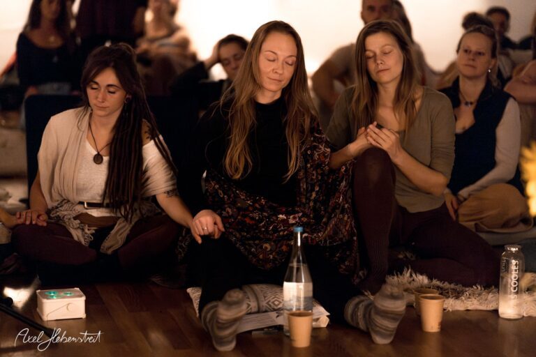 Drei Frauen im Yoga-Sitz verbinden sich in meditativer Atmosphäre während einer Veranstaltung – © Axel Hebenstreit