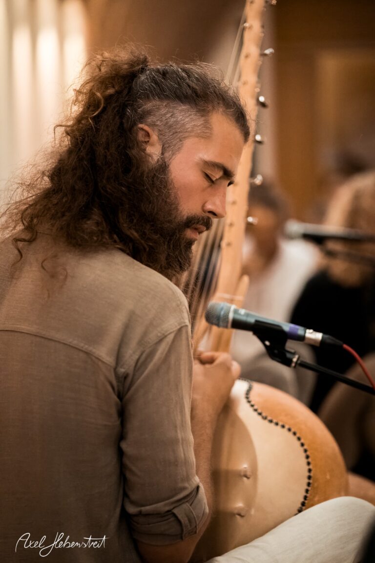Ein Musiker mit lockigem Haar spielt leidenschaftlich eine Kora in einer entspannten Atmosphäre. – © Axel Hebenstreit