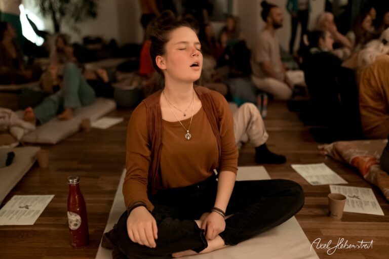 Junge Frau sitzt meditierend in einer entspannten Atmosphäre während einer Yogastunde – © Axel Hebenstreit