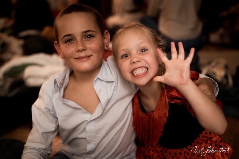 Lächelnde Kinder in festlicher Kleidung, die fröhlich miteinander posieren. – © Axel Hebenstreit
