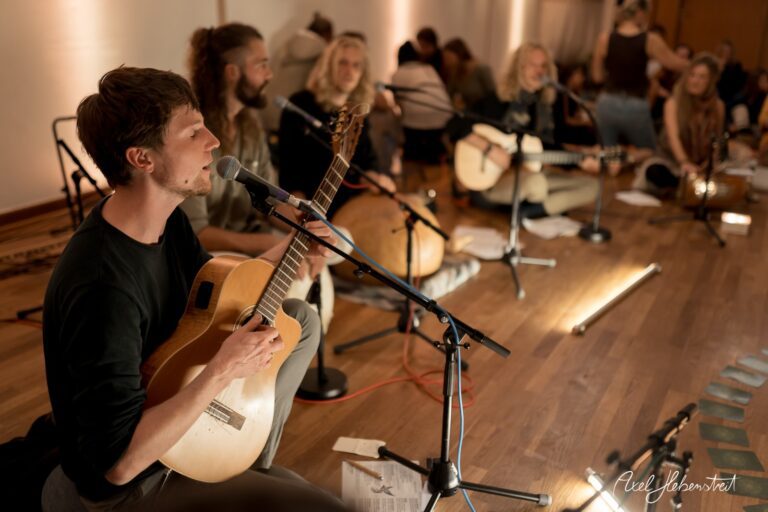 Musiker mit Akustikgitarre und Gesang in einer entspannten Atmosphäre während einer Veranstaltung. – © Axel Hebenstreit