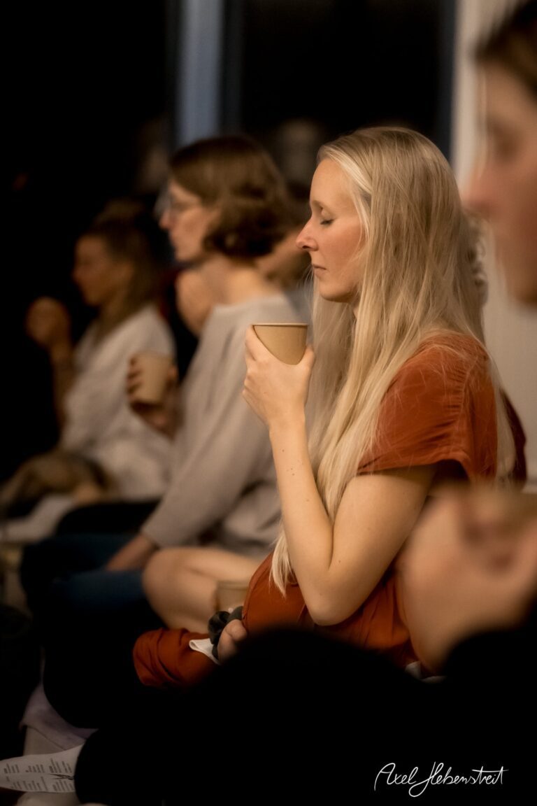 Eine Frau mit langem Haar hält einen Becher, während sie in einem meditativen Moment sitzt – © Axel Hebenstreit.