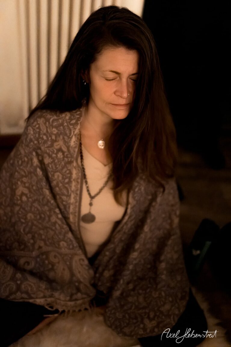 Frau mit geschlossenen Augen und Umhang meditiert in entspannter Atmosphäre. – © Axel Hebenstreit