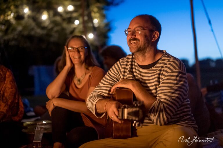 Gemütliche Abendstimmung am Lagerfeuer mit musikalischer Unterhaltung und fröhlichen Gesichtern – © Axel Hebenstreit