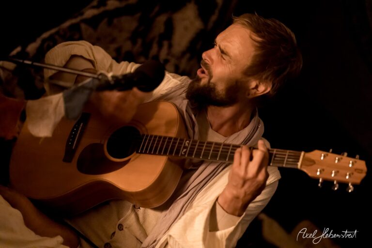 Musiker spielt leidenschaftlich Gitarre im warmen Licht eines Zeltes bei einer intimen Veranstaltung – © Axel Hebenstreit