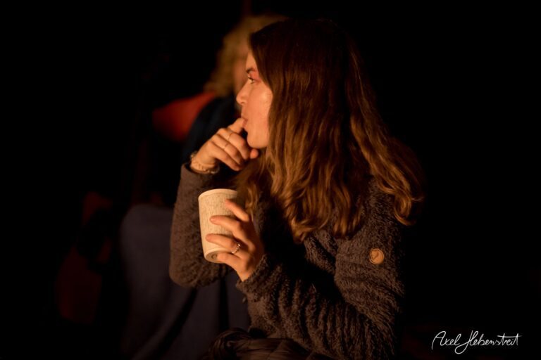 Eine nachdenkliche Frau mit einer Tasse in der Hand sitzt im Dunkeln und genießt die ruhige Lagerfeuerstimmung – © Axel Hebenstreit