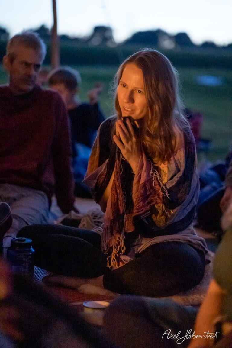 Eine nachdenkliche Frau sitzt im Kerzenlicht und spricht in einer entspannten Festivalatmosphäre – © Axel Hebenstreit