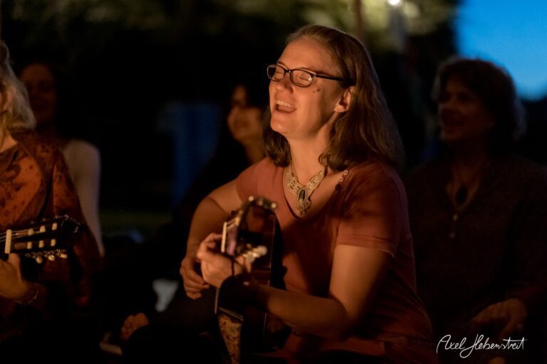 Eine lächelnde Frau spielt in der Abenddämmerung Gitarre und schafft eine entspannte, harmonische Atmosphäre – © Axel Hebenstreit