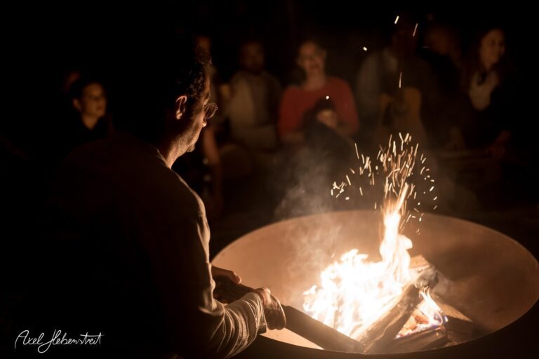 Ein Mann sitzt am Lagerfeuer, während Funken in die Nacht aufsteigen und eine warme Atmosphäre entsteht – © Axel Hebenstreit