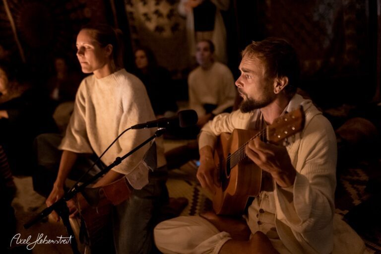 Menschen sitzen in einer meditativen Atmosphäre, während einer Gitarre spielt und die andere zuhört – © Axel Hebenstreit.