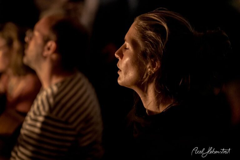 Frau in meditativer Haltung, umgeben von sanftem Licht, während einer entspannten Konzertatmosphäre – © Axel Hebenstreit