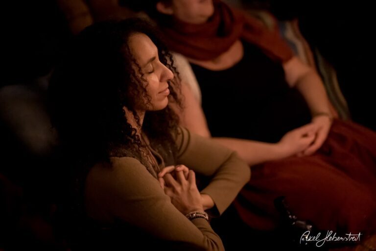 Frau mit geschlossenen Augen und gefalteten Händen in meditativem Zustand, umgeben von warmem Licht – © Axel Hebenstreit