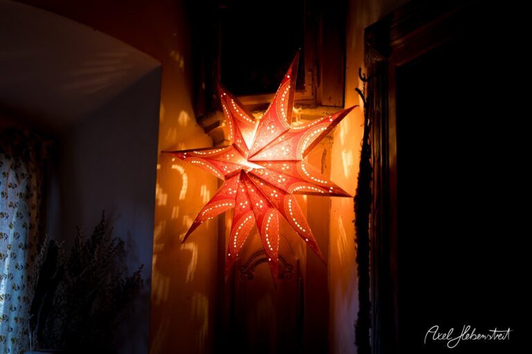 Leuchtender rot-weißer Weihnachtsstern an der Wand, der warmes Licht und festliche Stimmung in einem Raum verbreitet – © Axel Hebenstreit