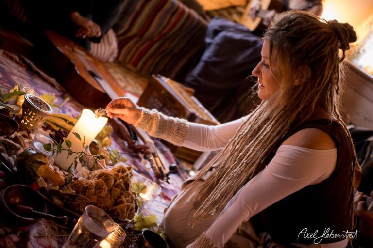 Eine Frau mit Dreadlocks zündet eine Kerze an, umgeben von Naturmaterialien und einer warmen, einladenden Atmosphäre – © Axel Hebenstreit.