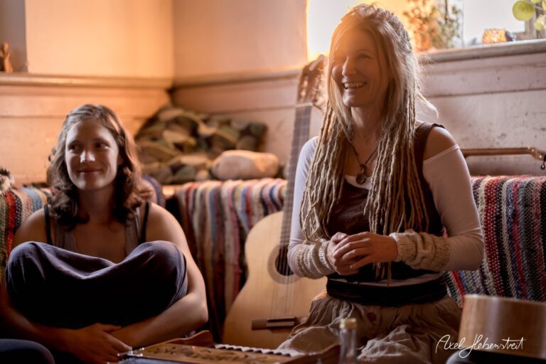 Zwei Frauen in gemütlicher Atmosphäre, lächelnd beim Musizieren in einem harmonischen Raum – © Axel Hebenstreit.