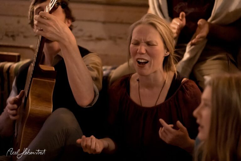 Eine emotionale Gesangsszene mit einer Frau und einem Gitarristen in einer gemütlichen Umgebung – © Axel Hebenstreit