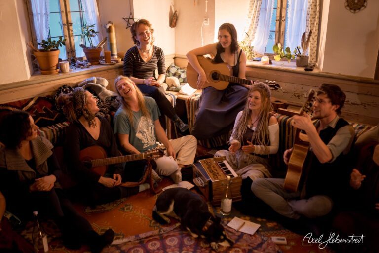 Frauen und Männer sitzen in einem gemütlichen Raum und musizieren zusammen, während eine entspannte Stimmung herrscht – © Axel Hebenstreit