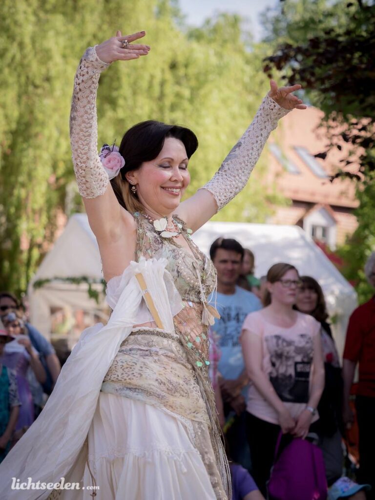 Tanzende Frau in eleganter Gewandung bei einem Festival, umgeben von faszinierten Zuschauern im Freien.
