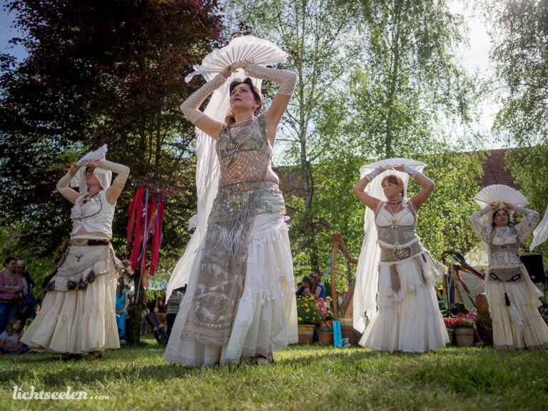 Tanzende Frauen in eleganten Kostümen und mit Fächern, während eines Festivals im Freien in Bayern.