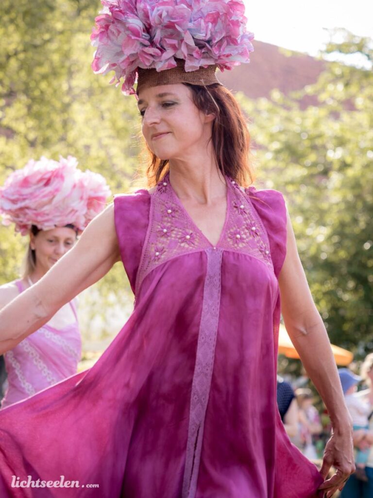 Frau in pinkem Kleid mit bezauberndem Kopfschmuck tanzt fröhlich auf einem Festival im Freien.